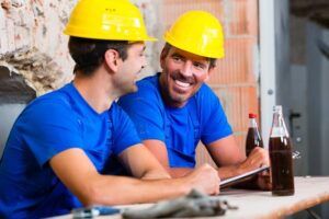 Builders having break on construction site sitting down drinking beverages